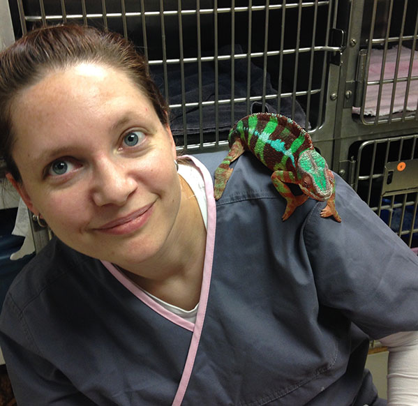 Bre, with long dark hair, wearing teal scrubs, is holding up a turtle and smiling.